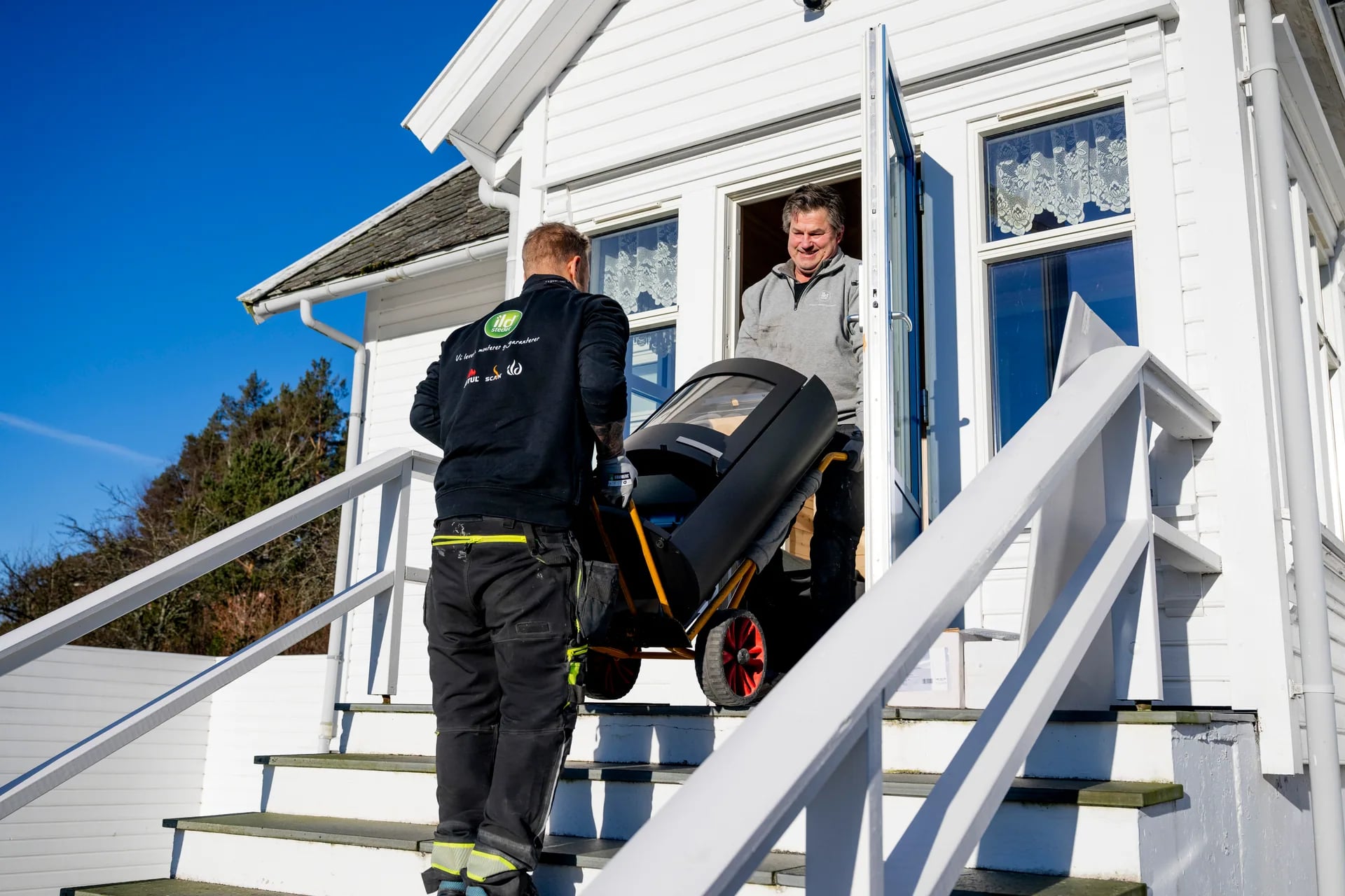 To montører leverer ny ovn opp trappa til kunde